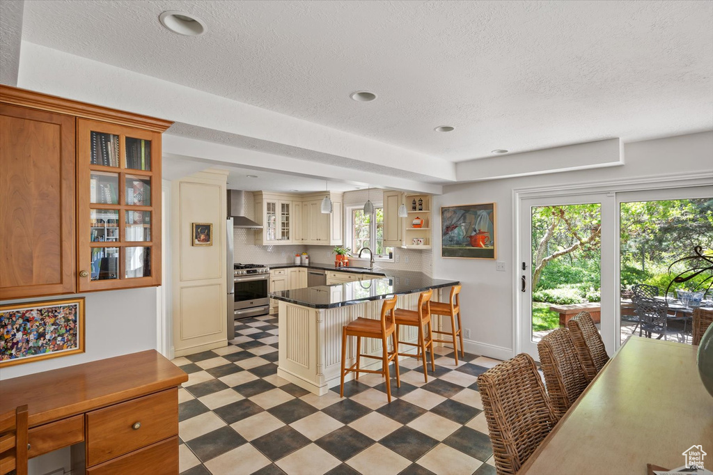 Kitchen featuring appliances with stainless steel finishes, wall chimney range hood, light floors, a peninsula, and a sink