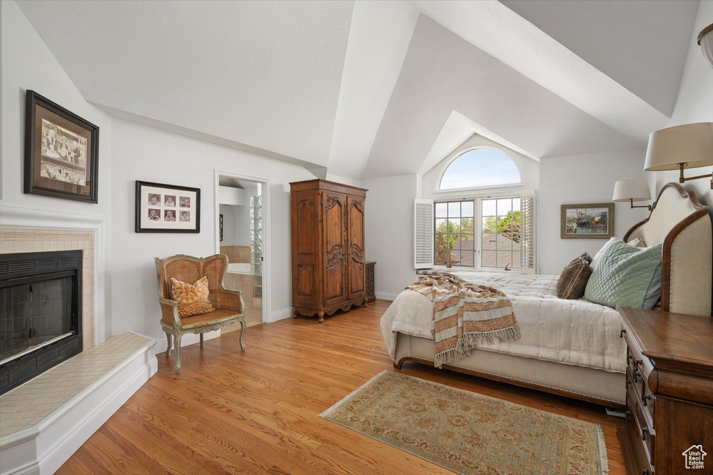 Bedroom with a fireplace, light wood-type flooring, lofted ceiling, and ensuite bath