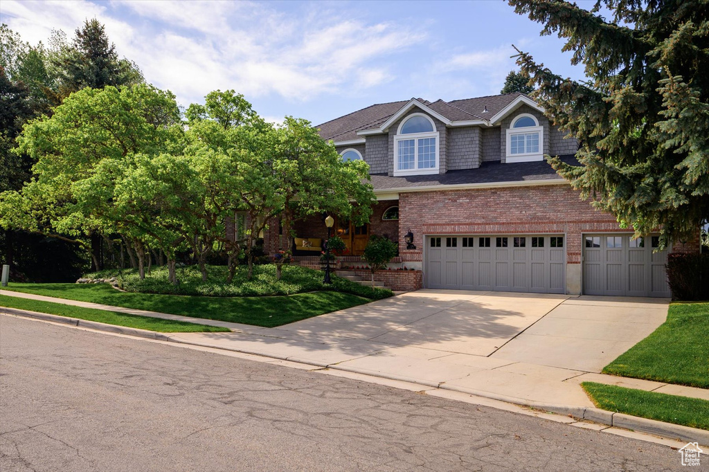 View of front of property with brick siding, concrete driveway, a garage, a shingled roof, and a front lawn