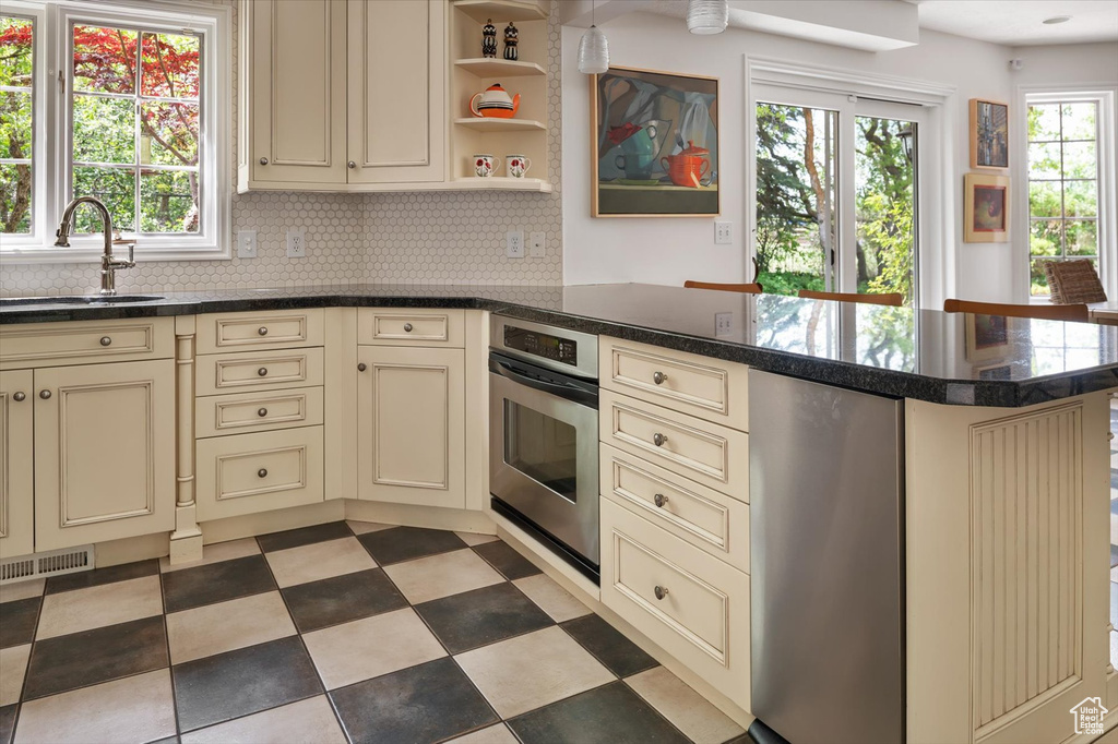 Kitchen featuring cream cabinets, a sink, a peninsula, stainless steel oven, and backsplash
