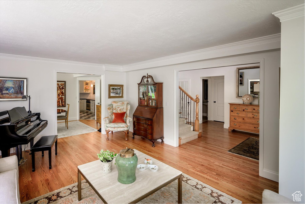 Living room featuring ornamental molding, light wood-style flooring, stairway, and baseboards