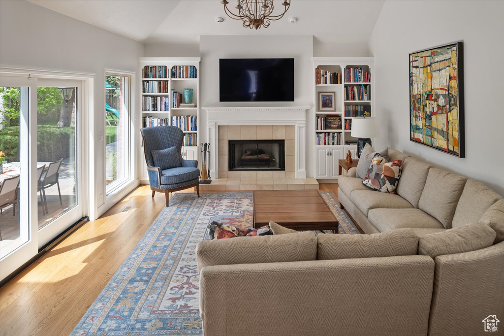 Living area with lofted ceiling, wood finished floors, a chandelier, a tiled fireplace, and built in shelves