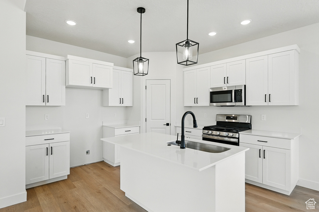 Kitchen featuring appliances with stainless steel finishes, a sink, light wood-type flooring, a center island with sink, and white cabinets