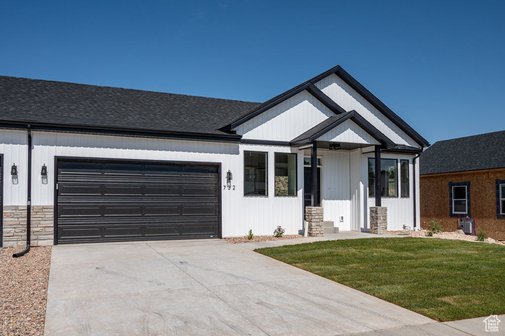 Modern inspired farmhouse featuring a garage, roof with shingles, stone siding, and a front yard