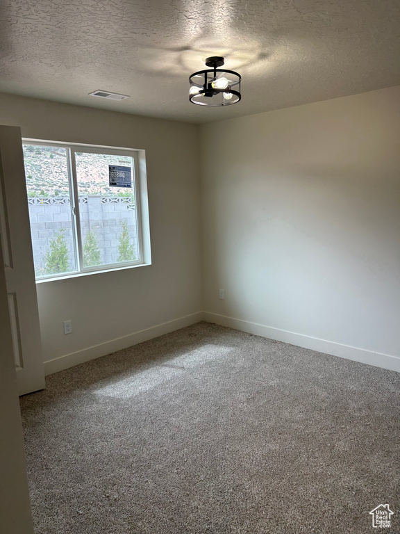 Carpeted spare room featuring a textured ceiling, baseboards, and a chandelier