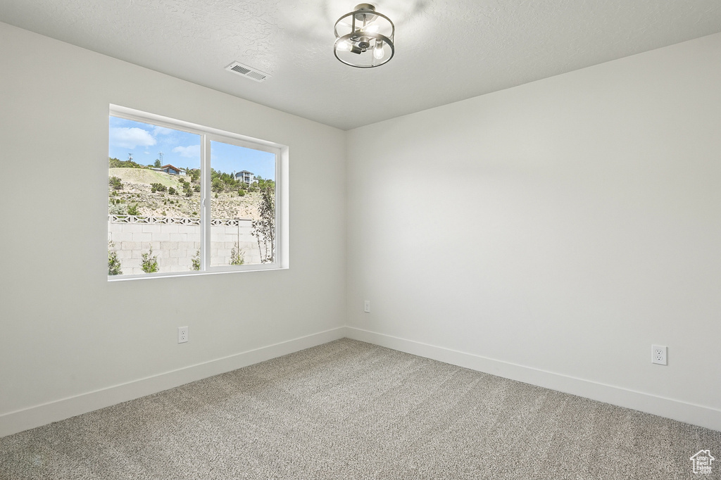Spare room featuring baseboards, carpet floors, a textured ceiling, and a chandelier