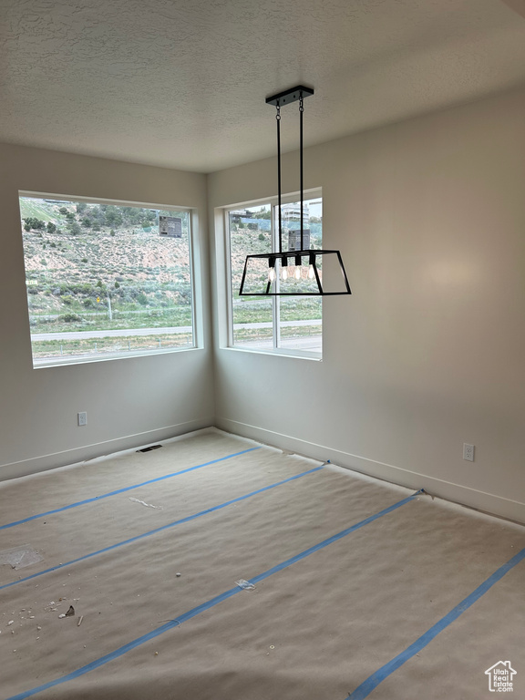 Unfurnished dining area featuring plenty of natural light, baseboards, and a textured ceiling