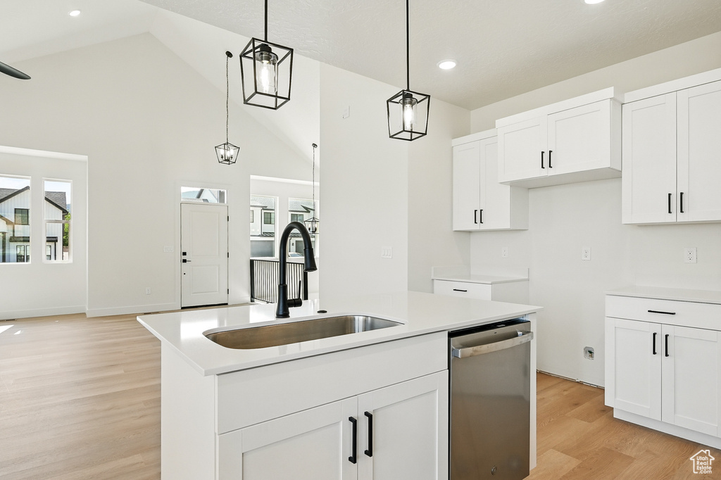 Kitchen featuring stainless steel dishwasher, a sink, light wood finished floors, pendant lighting, and white cabinetry