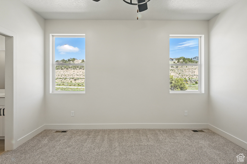 Carpeted empty room featuring a ceiling fan, baseboards, and a textured ceiling