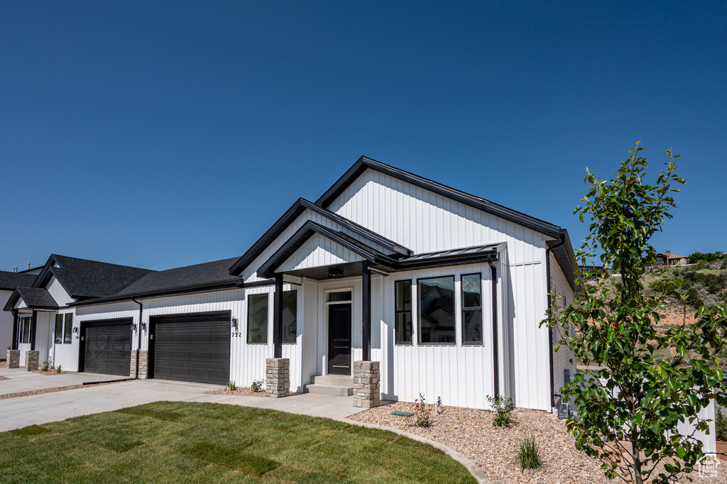 Modern inspired farmhouse featuring an attached garage, a front yard, concrete driveway, entry steps, and board and batten siding