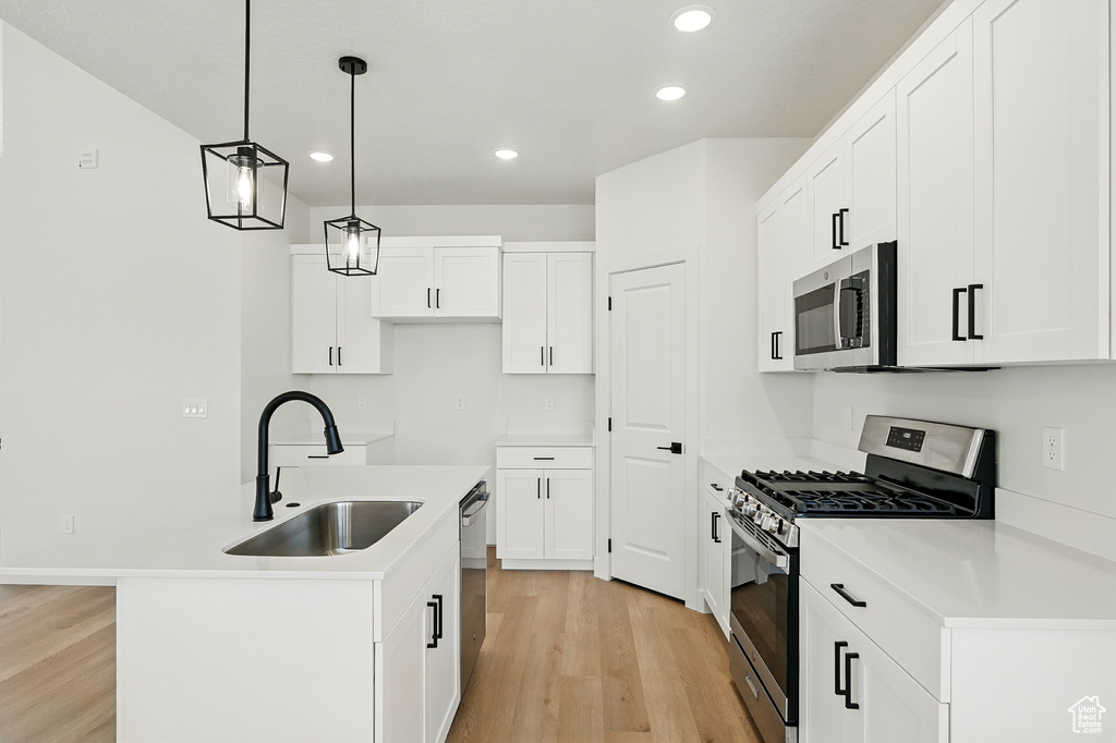 Kitchen with appliances with stainless steel finishes, a sink, light wood-style floors, recessed lighting, and a kitchen island with sink