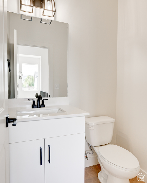 Half bathroom featuring toilet, vanity, baseboards, and wood finished floors