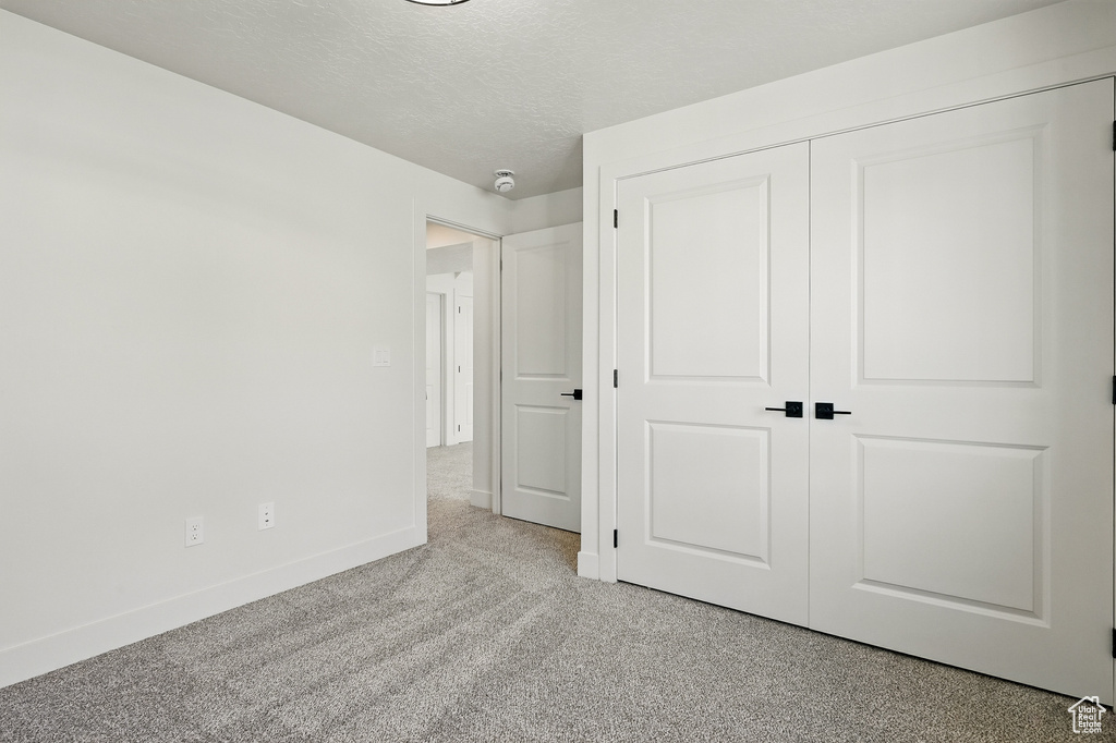 Unfurnished bedroom with baseboards, a closet, a textured ceiling, and light colored carpet