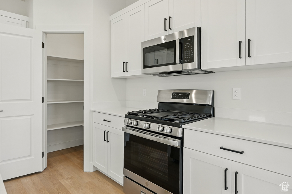 Kitchen with stainless steel appliances, light wood-style floors, light countertops, and white cabinetry