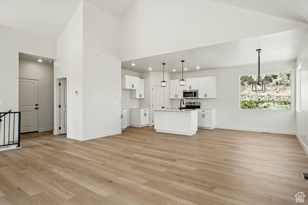 Unfurnished living room featuring light wood-style floors, a high ceiling, baseboards, a sink, and recessed lighting