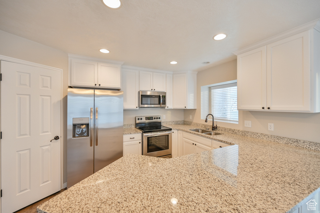 Kitchen with appliances with stainless steel finishes, a sink, light stone counters, white cabinets, and recessed lighting