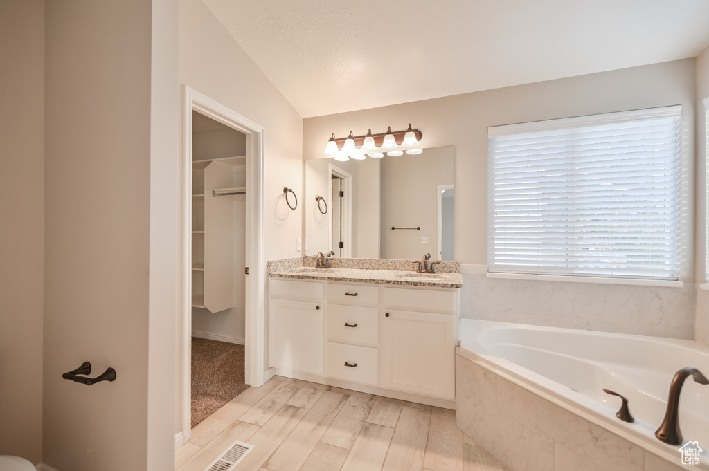 Full bath featuring double vanity, a garden tub, a walk in closet, and wood finished floors
