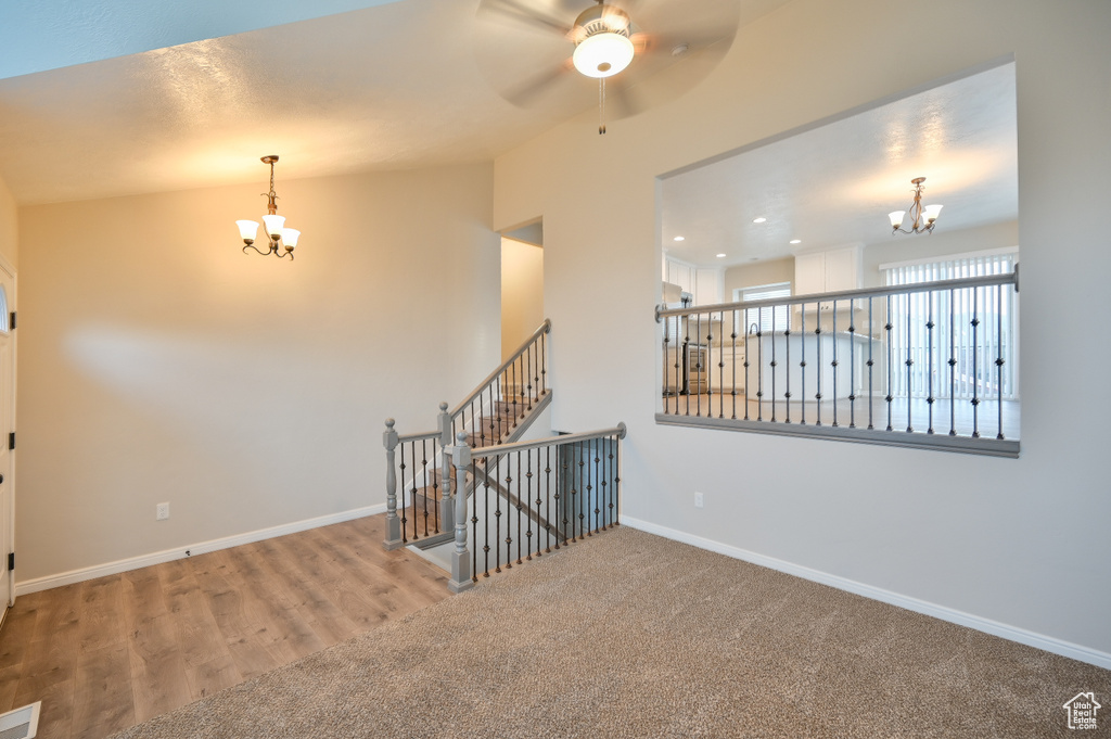 Spare room featuring a chandelier, baseboards, a ceiling fan, vaulted ceiling, and wood finished floors