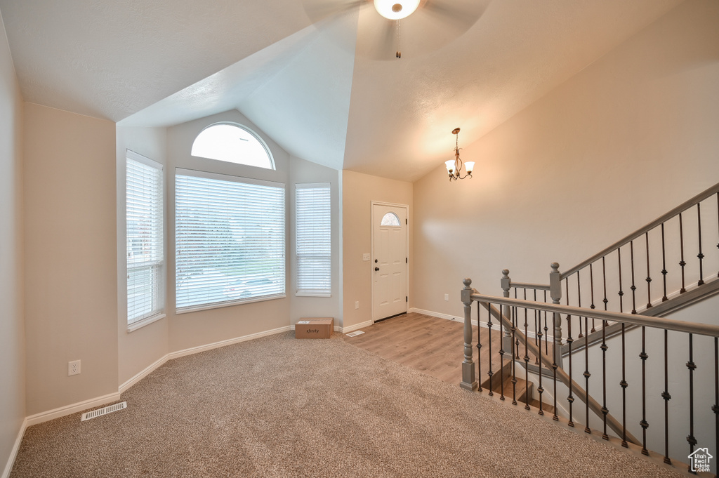 Carpeted foyer with lofted ceiling, plenty of natural light, a chandelier, a ceiling fan, and baseboards