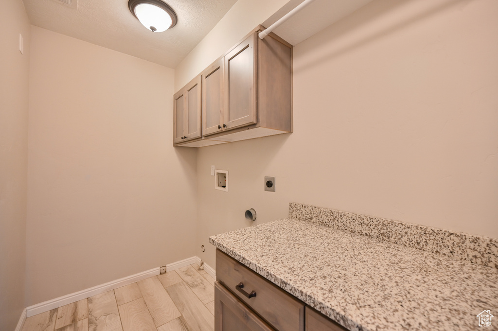 Laundry room featuring hookup for an electric dryer, hookup for a washing machine, baseboards, cabinet space, and light wood finished floors