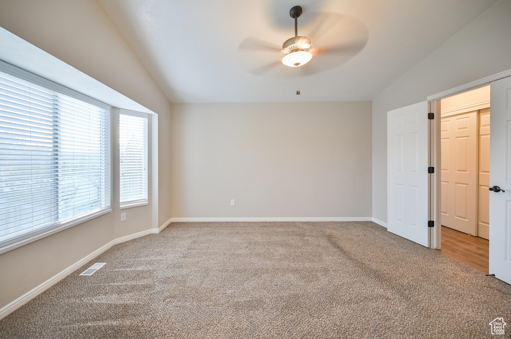 Unfurnished bedroom with vaulted ceiling, light carpet, baseboards, and a ceiling fan