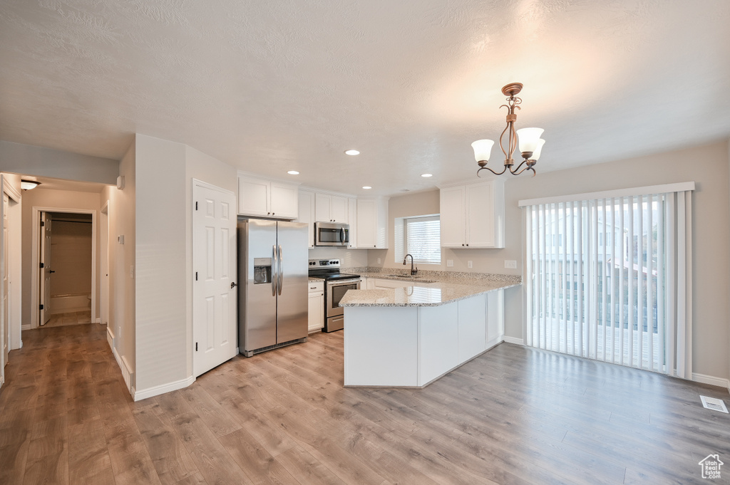 Kitchen with stainless steel appliances, a peninsula, a sink, a chandelier, and white cabinetry