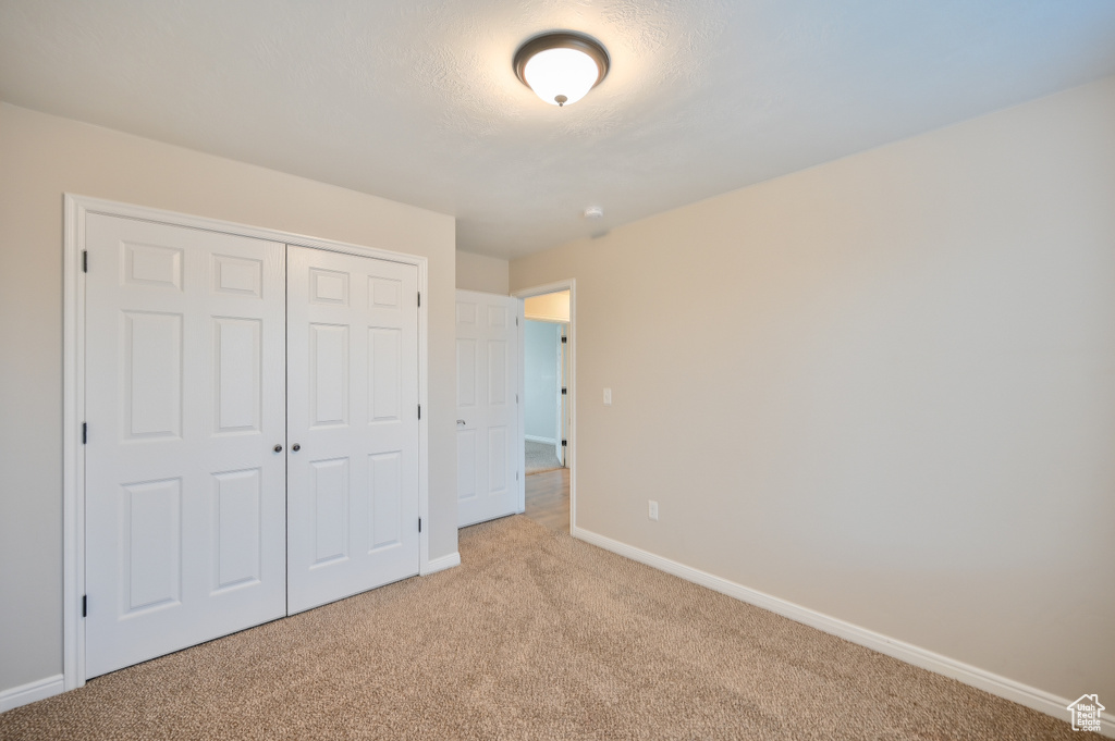 Unfurnished bedroom with light colored carpet, baseboards, and a closet