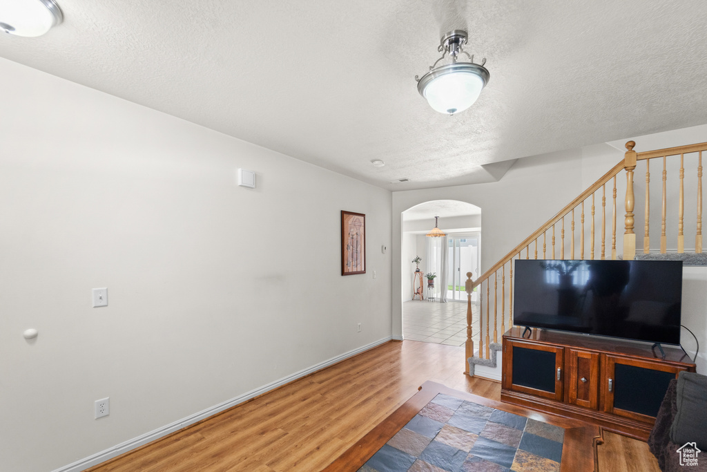 Living room with arched walkways, wood finished floors, a textured ceiling, stairs, and baseboards