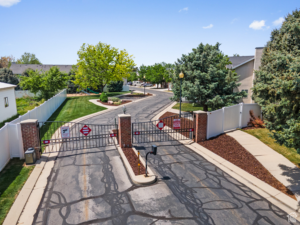 View of asphalt street featuring street lights, a gate, traffic signs, curbs, and a gated entry