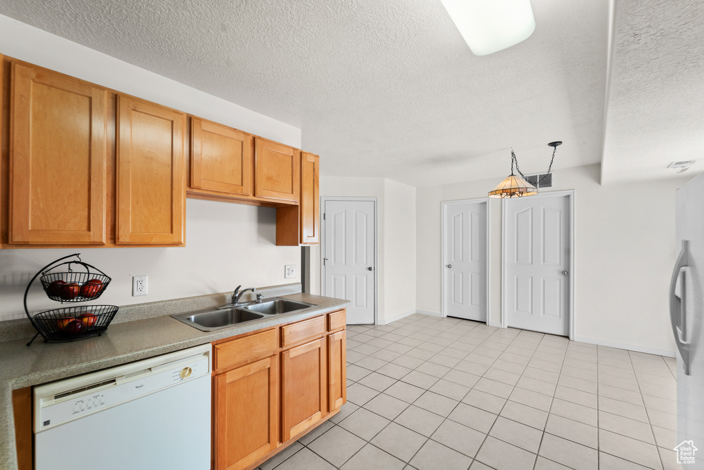 Kitchen featuring white appliances, a sink, a textured ceiling, light tile patterned floors, and baseboards