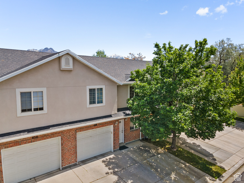View of property with brick siding, a shingled roof, stucco siding, concrete driveway, and an attached garage