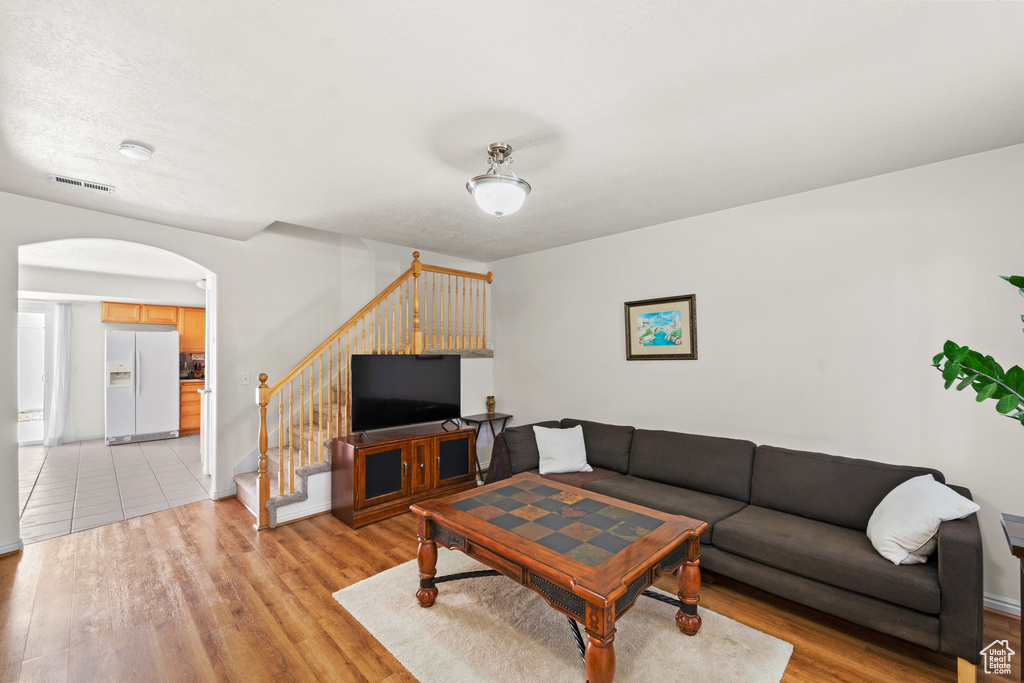 Living area featuring arched walkways, light wood-style flooring, stairs, and baseboards