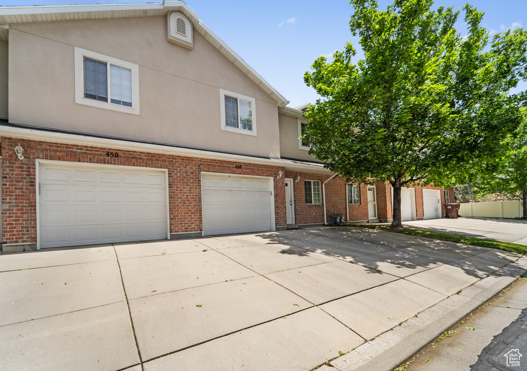Townhome / multi-family property with driveway, a garage, brick siding, and stucco siding