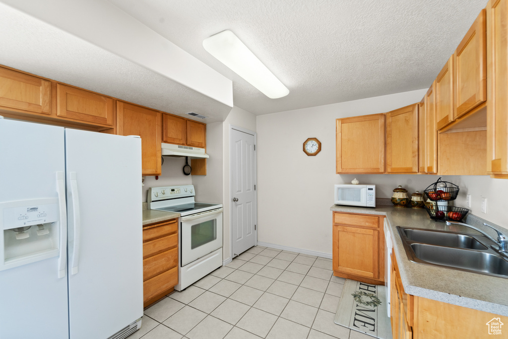 Kitchen featuring white appliances, under cabinet range hood, a sink, light tile patterned flooring, and light countertops
