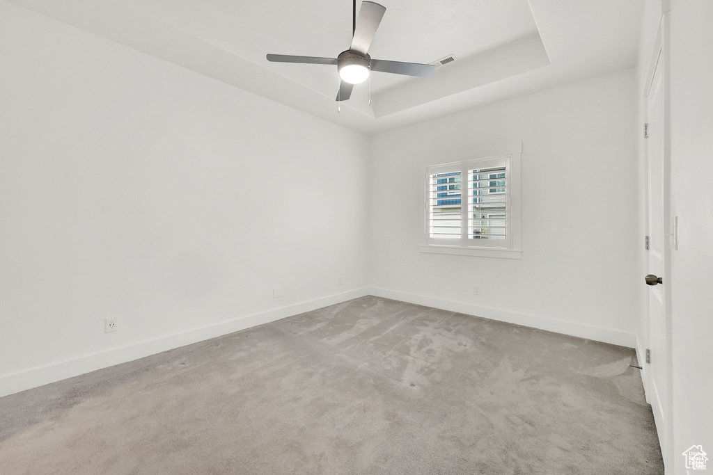 Empty room with carpet floors, baseboards, a tray ceiling, and a ceiling fan