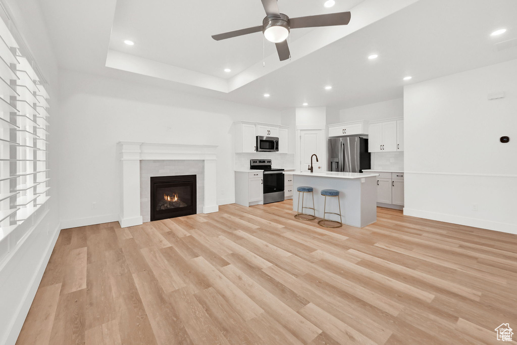 Unfurnished living room with a ceiling fan, light wood-type flooring, a glass covered fireplace, recessed lighting, and a tray ceiling