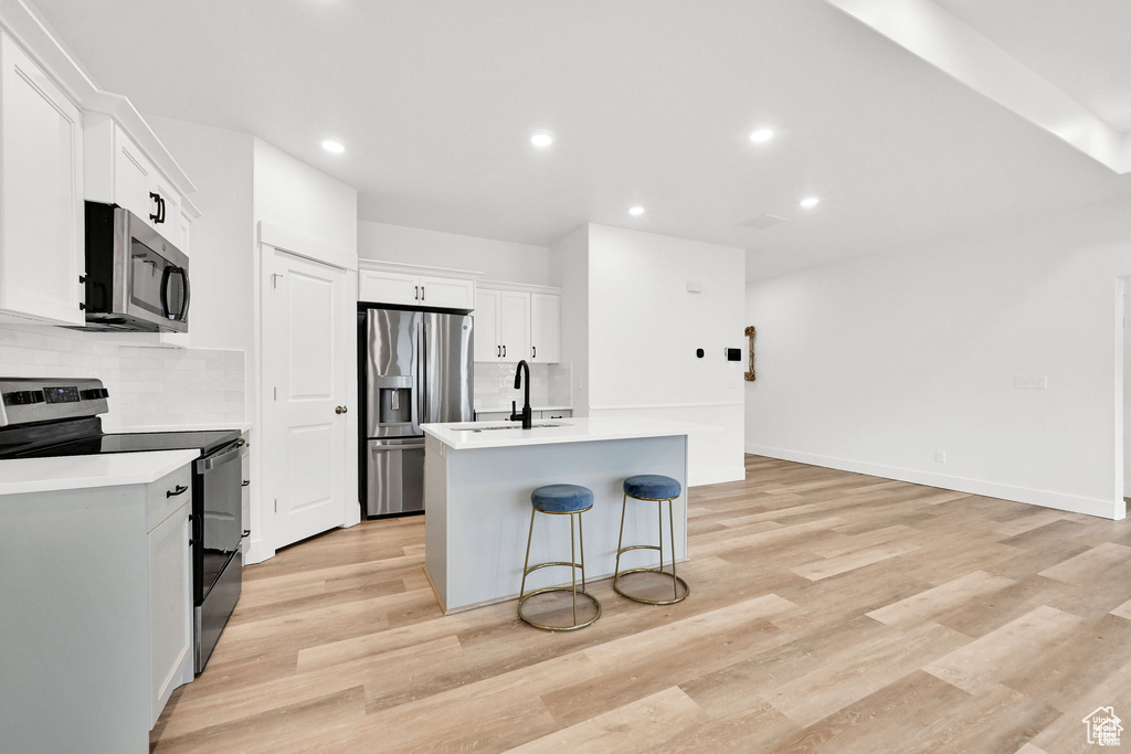 Kitchen featuring appliances with stainless steel finishes, decorative backsplash, a kitchen island with sink, light countertops, and recessed lighting