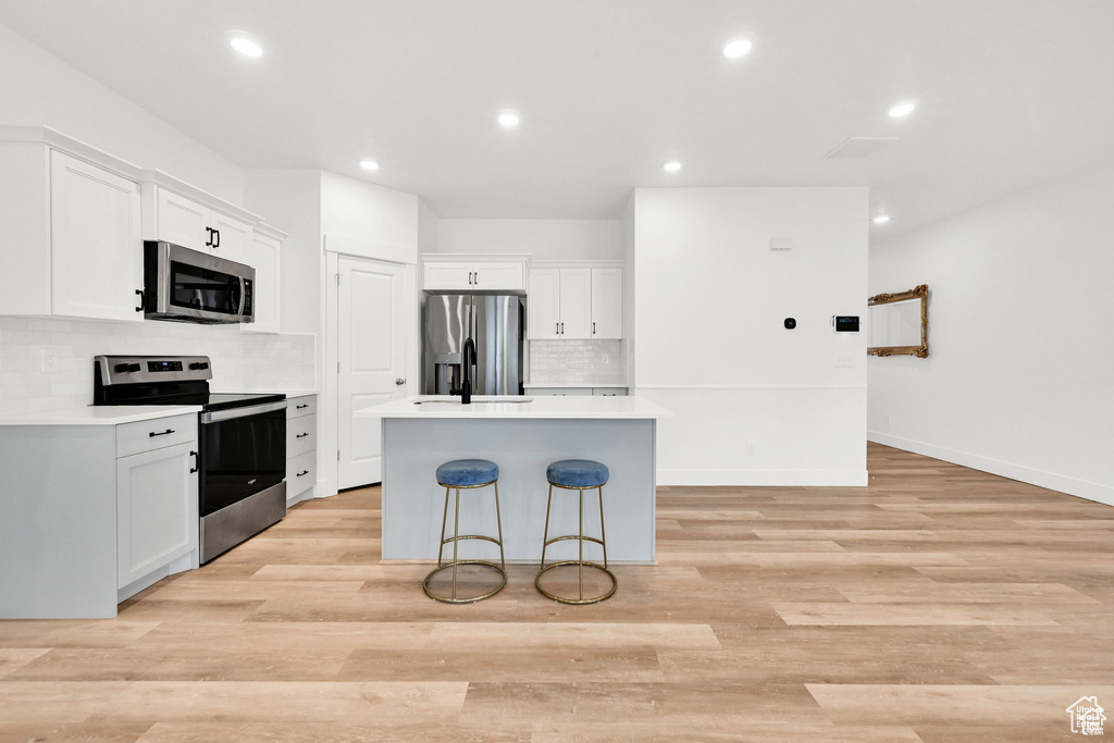 Kitchen featuring appliances with stainless steel finishes, a kitchen island, backsplash, white cabinetry, and light countertops