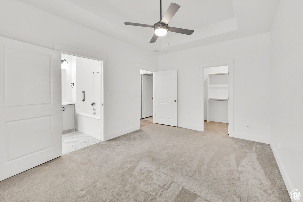 Unfurnished bedroom with baseboards, a walk in closet, ensuite bath, light carpet, and a closet