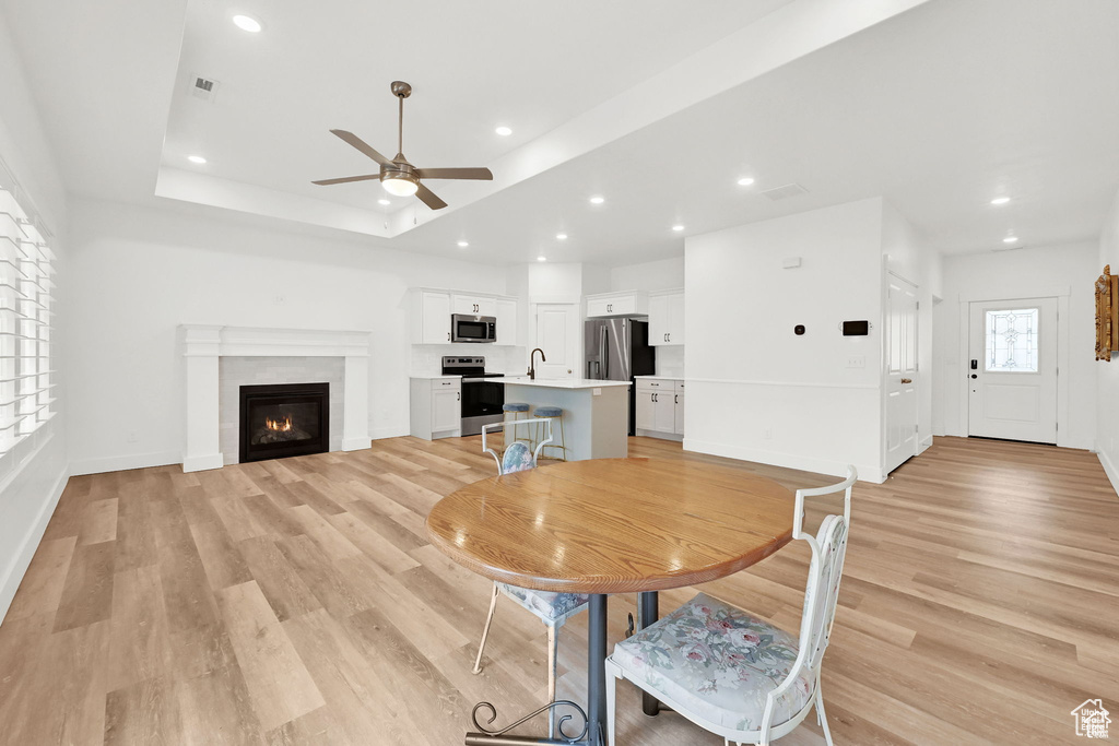 Dining space featuring a ceiling fan, light wood-type flooring, baseboards, a glass covered fireplace, and recessed lighting