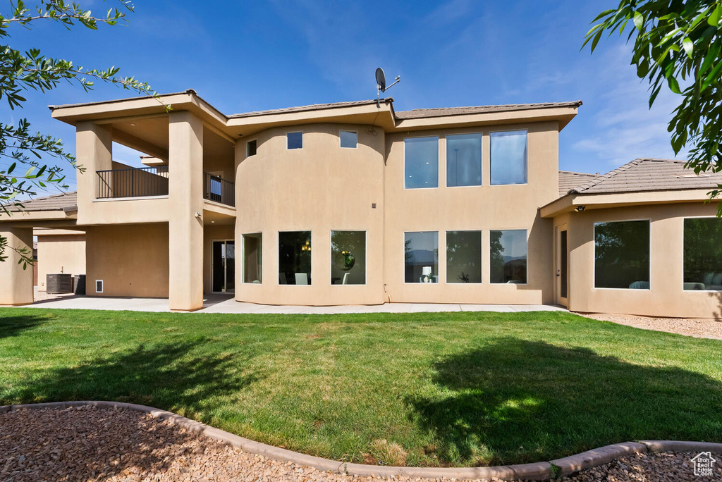 Rear view of house with a balcony, stucco siding, a lawn, a patio, and central air condition unit