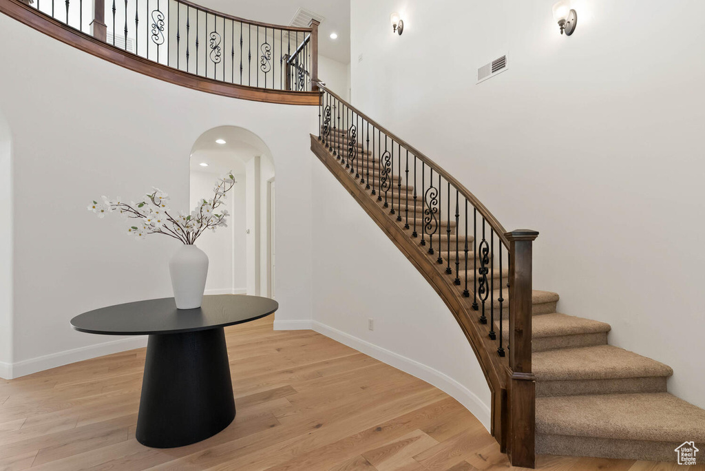 Stairway featuring wood finished floors, baseboards, arched walkways, and a towering ceiling