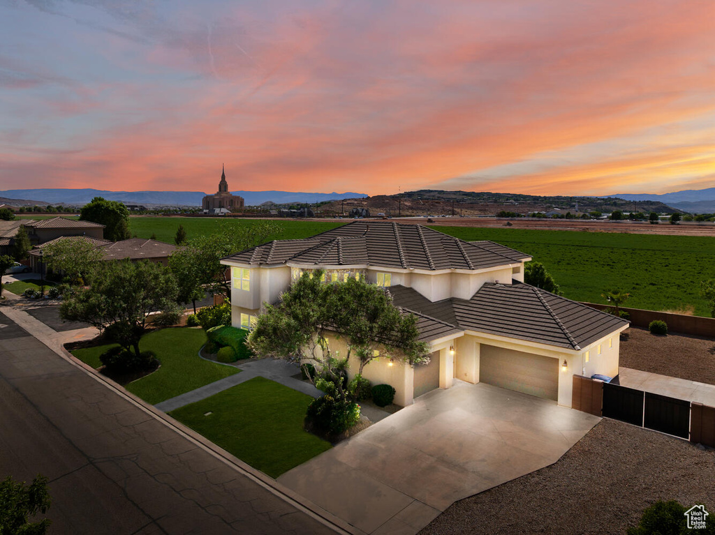 View of front facade featuring a garage, driveway, stucco siding, a tiled roof, and a rural view