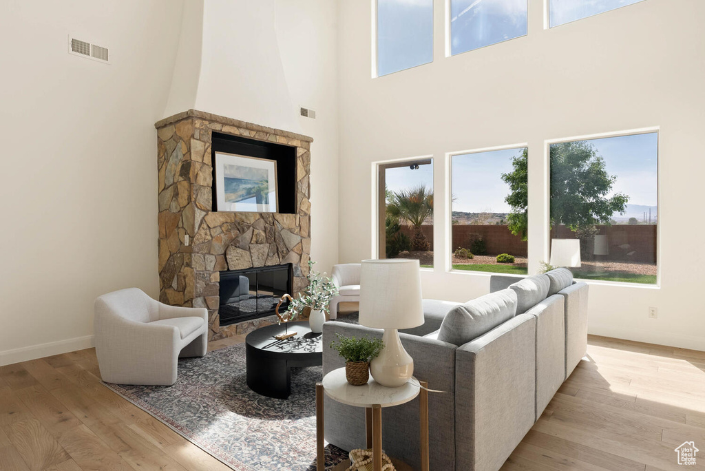 Living room featuring a stone fireplace, plenty of natural light, a high ceiling, and light wood-style floors