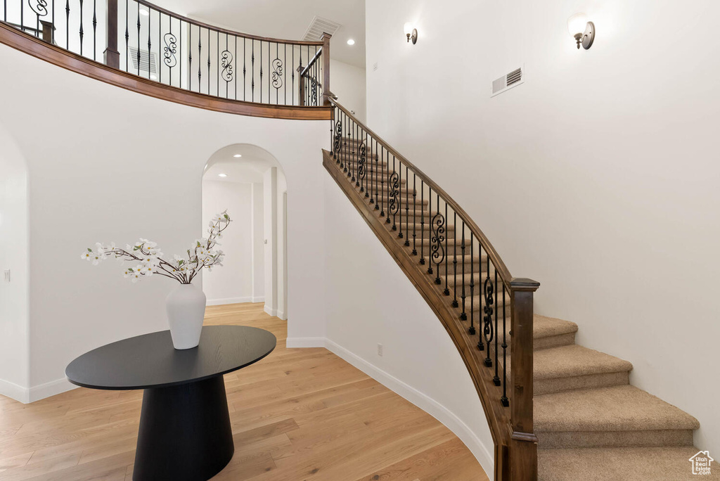 Staircase featuring wood finished floors, arched walkways, baseboards, and a high ceiling