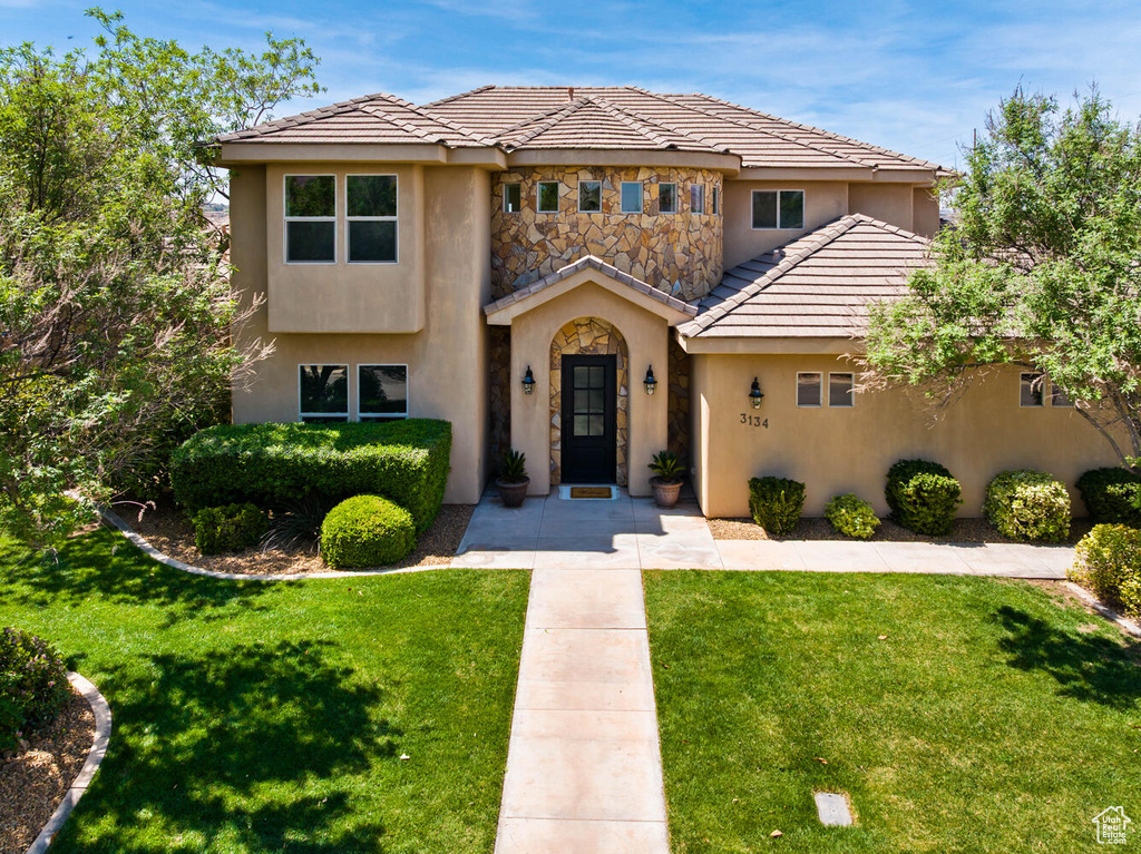 View of front of property featuring stucco siding, a front yard, a tiled roof, and stone siding