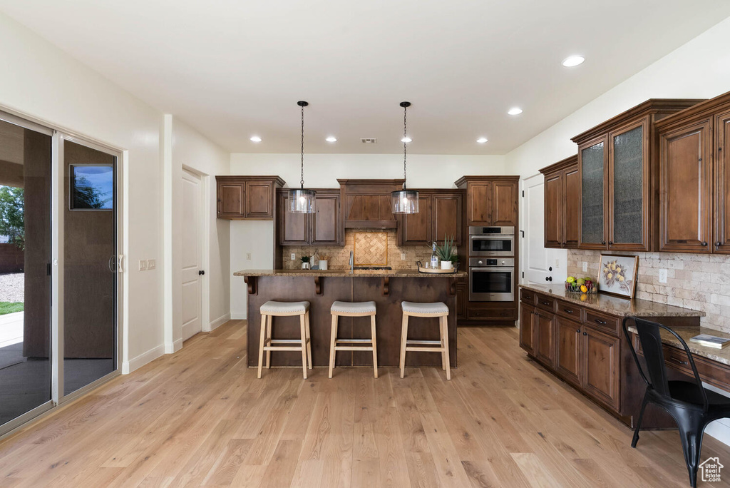 Kitchen featuring stainless steel double oven, decorative backsplash, a breakfast bar, light wood-style flooring, and glass insert cabinets