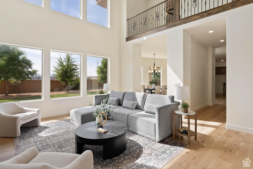 Living room featuring a towering ceiling, healthy amount of natural light, a chandelier, light wood-type flooring, and baseboards