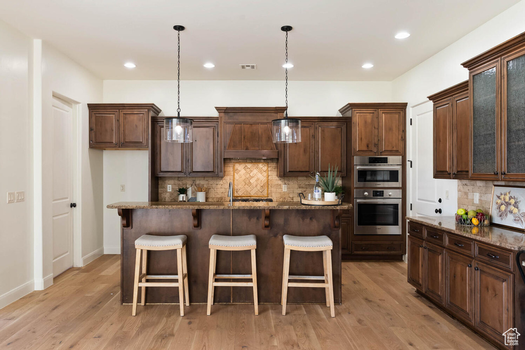 Kitchen featuring stainless steel double oven, premium range hood, tasteful backsplash, a breakfast bar area, and recessed lighting