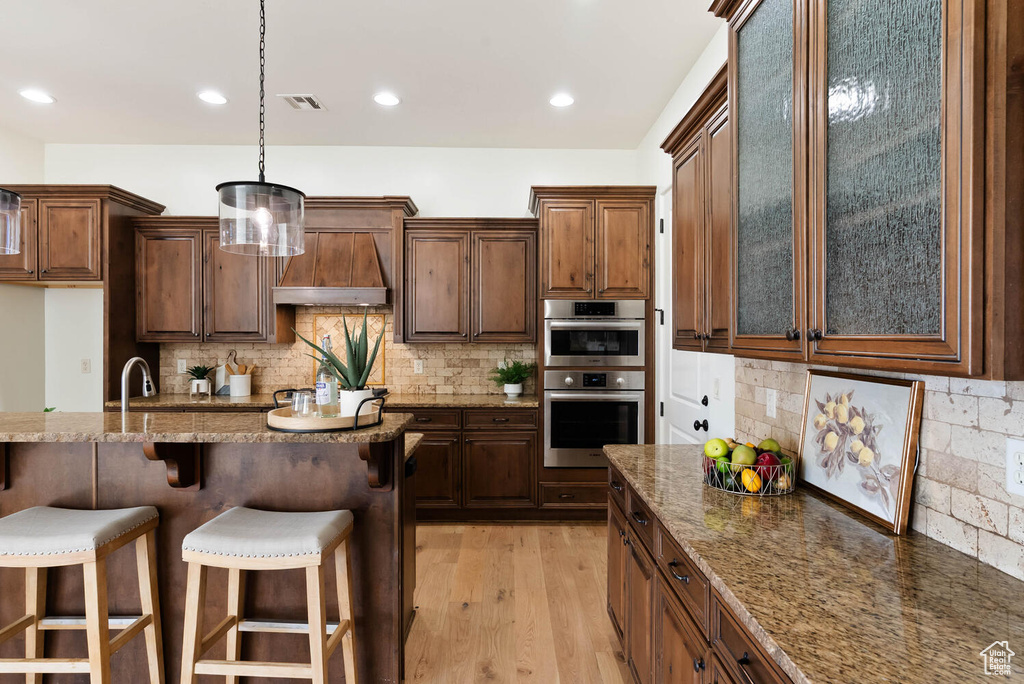 Kitchen with a kitchen breakfast bar, tasteful backsplash, light wood-type flooring, dark stone counters, and double oven